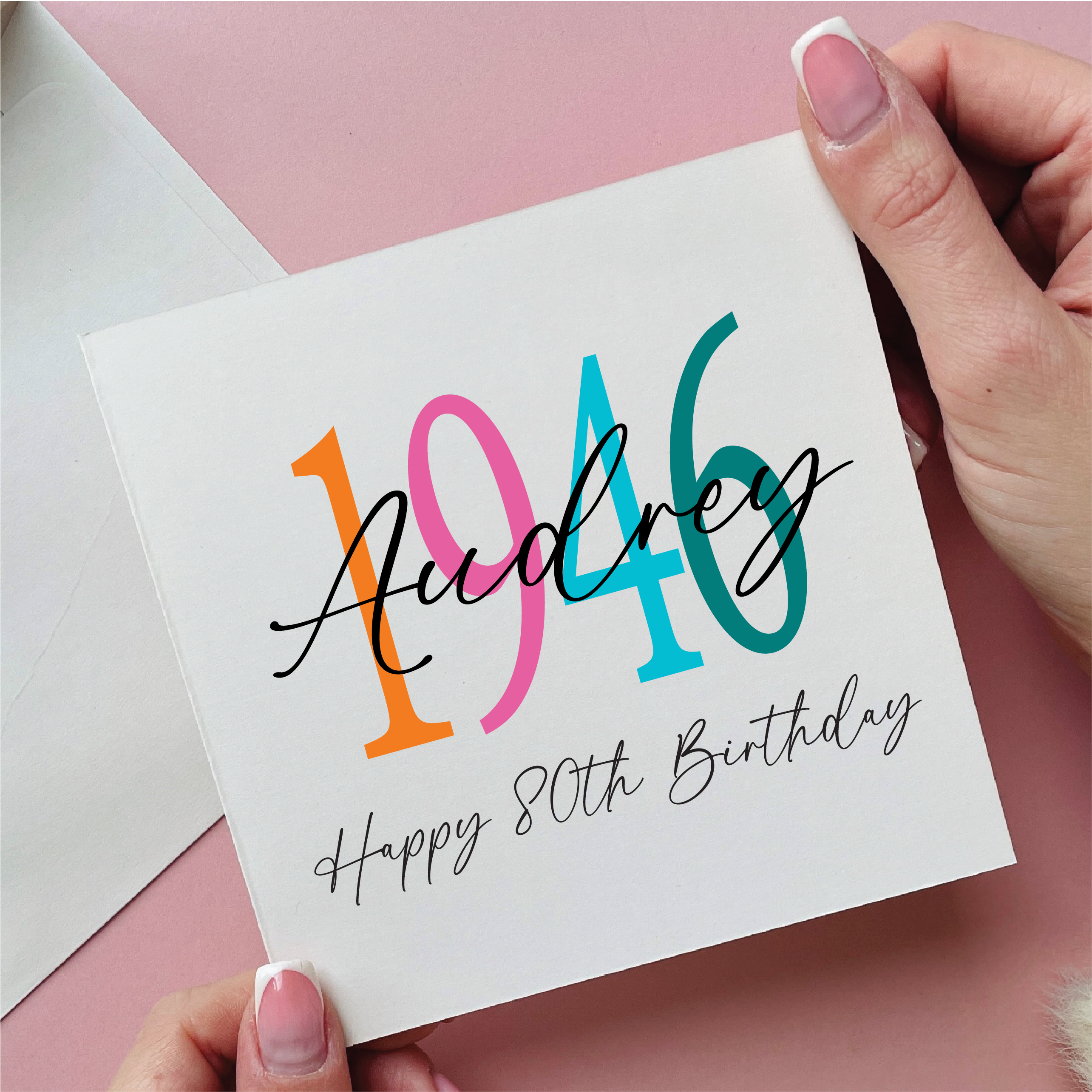 Hand holding a card with 'Audrey 1946 Happy 80th Birthday' text on a pink background