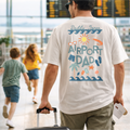 Man wearing a 'Airport Dad' t-shirt in an airport with children in the background.