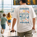 Man wearing a 'Airport Dad' t-shirt in an airport with children in the background.