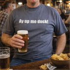 Man wearing a t-shirt with 'Ay up me duck!' text, holding a beer in a bar setting.