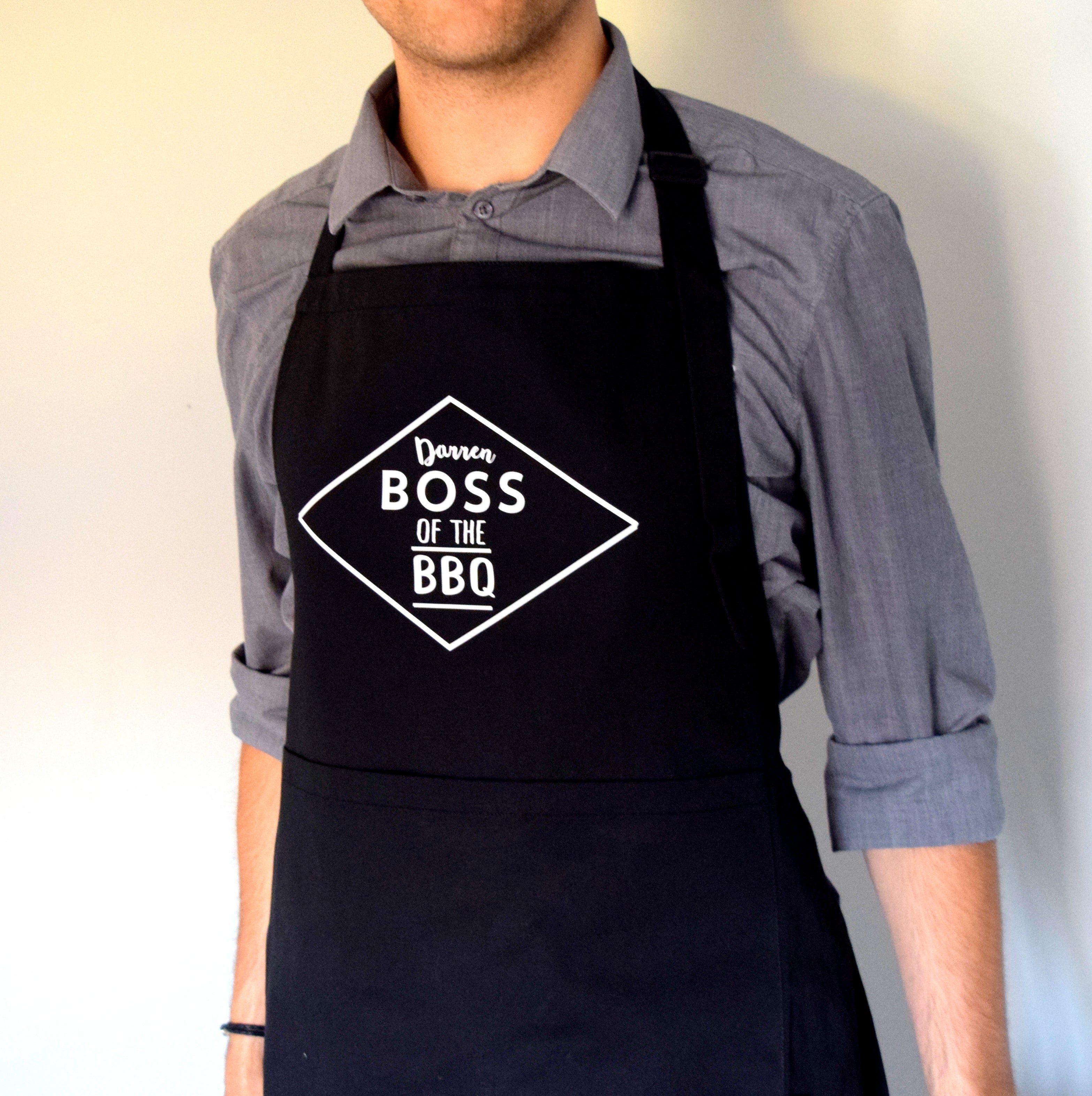 Person wearing a black apron with 'Boss of the BBQ' text on a plain background