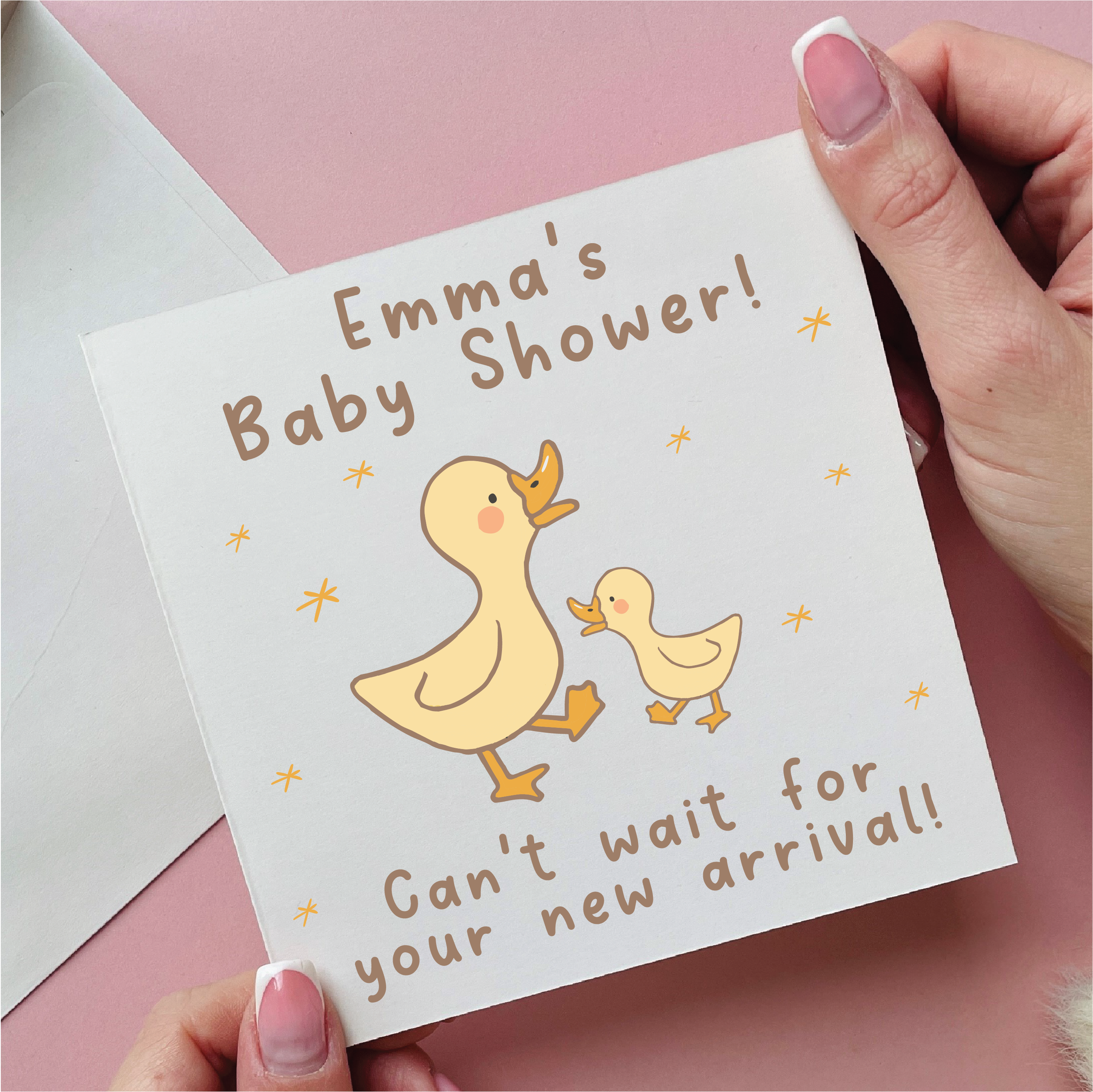 Baby shower card with ducks and text held by a hand on a pink background