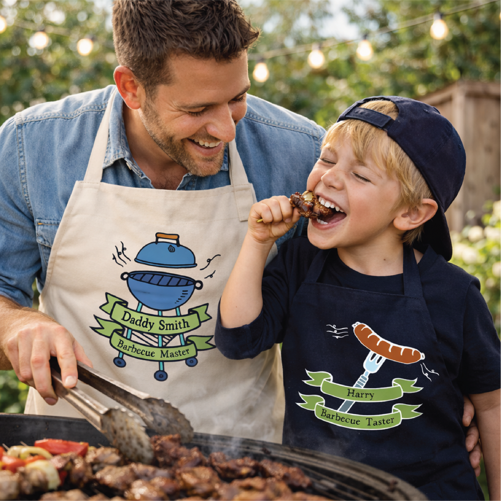 Man and child grilling outdoors, both wearing aprons with barbecue-themed designs.