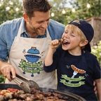 Man and child grilling outdoors, both wearing aprons with barbecue-themed designs.