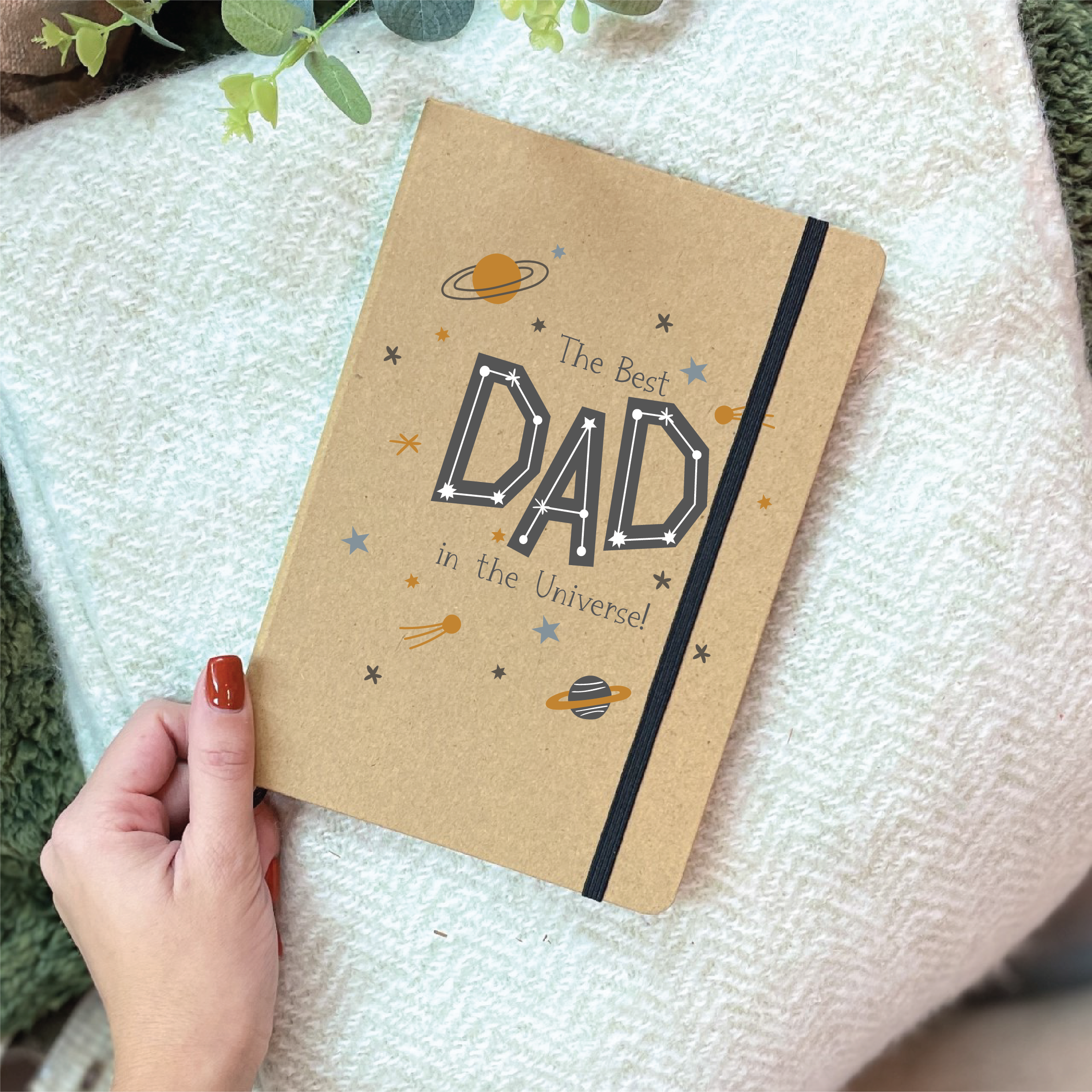 Notebook with 'The Best Dad in the Universe' text held by a hand on a textured surface.