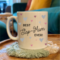 Mug with 'Best Step-Mum Ever!' text on a wooden table with a cozy background