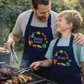 Man and child grilling outdoors wearing personalized aprons.