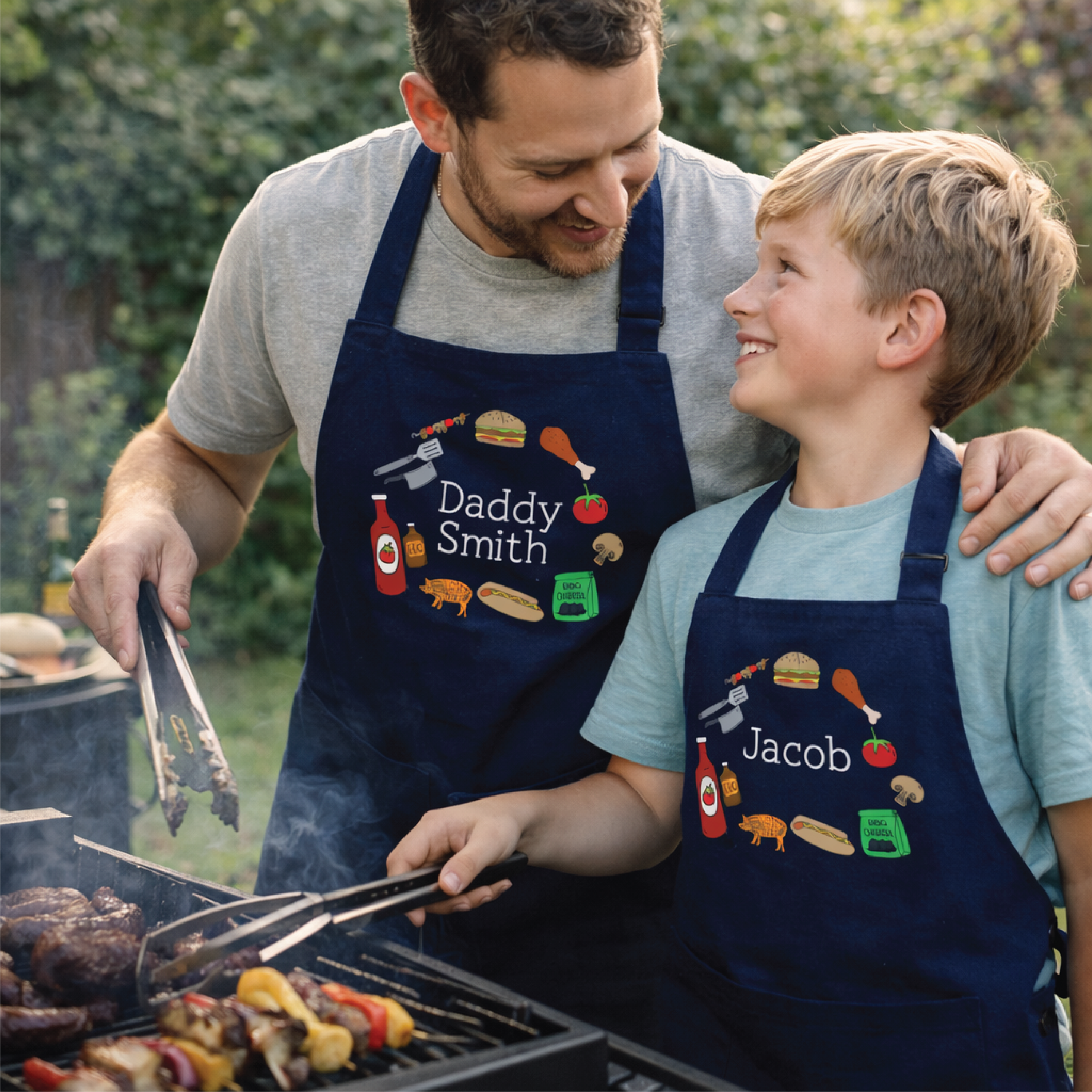Man and child grilling outdoors wearing personalized aprons.