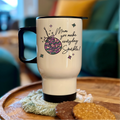 White travel mug with black handle and text on a wooden surface with cookies