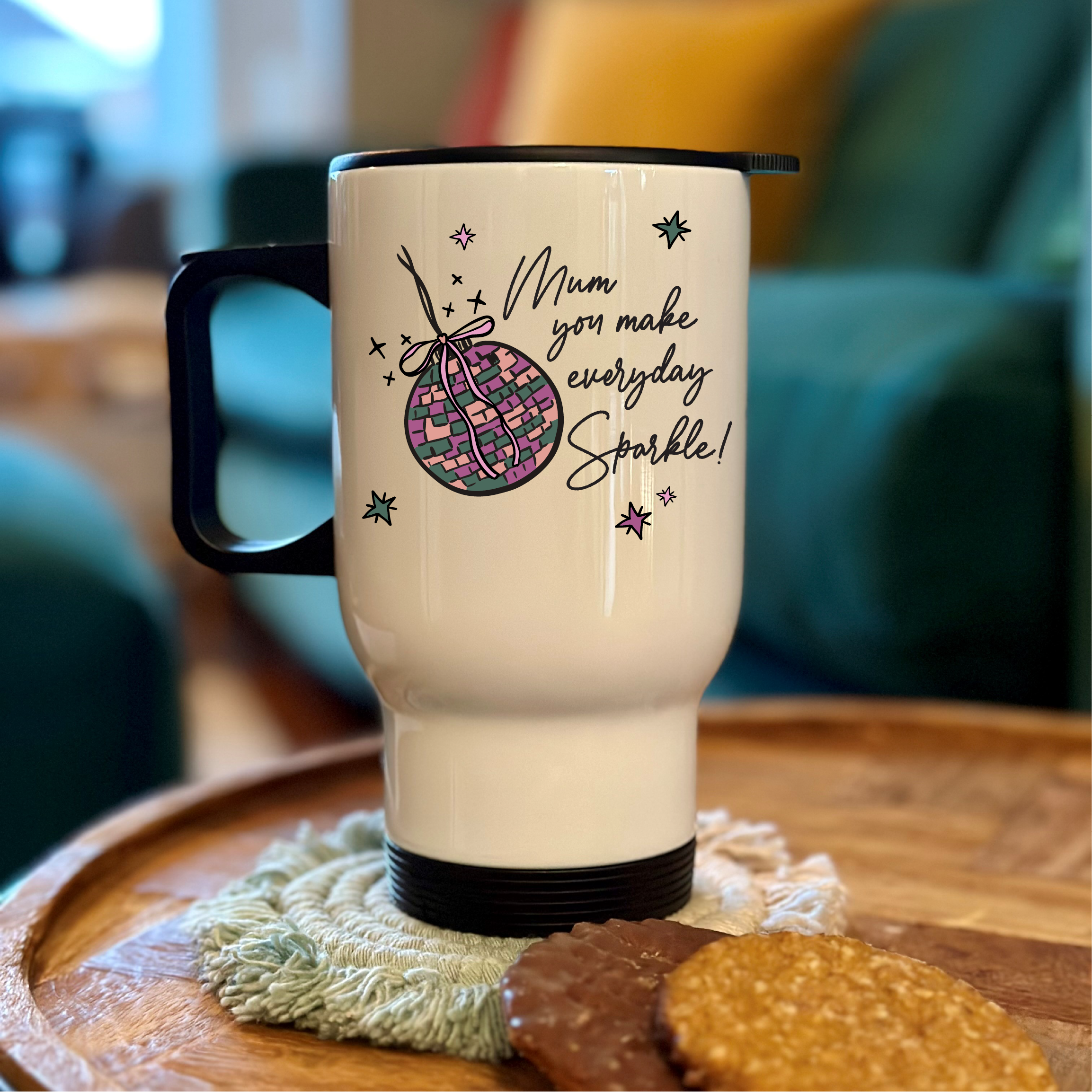White travel mug with black handle and text on a wooden surface with cookies