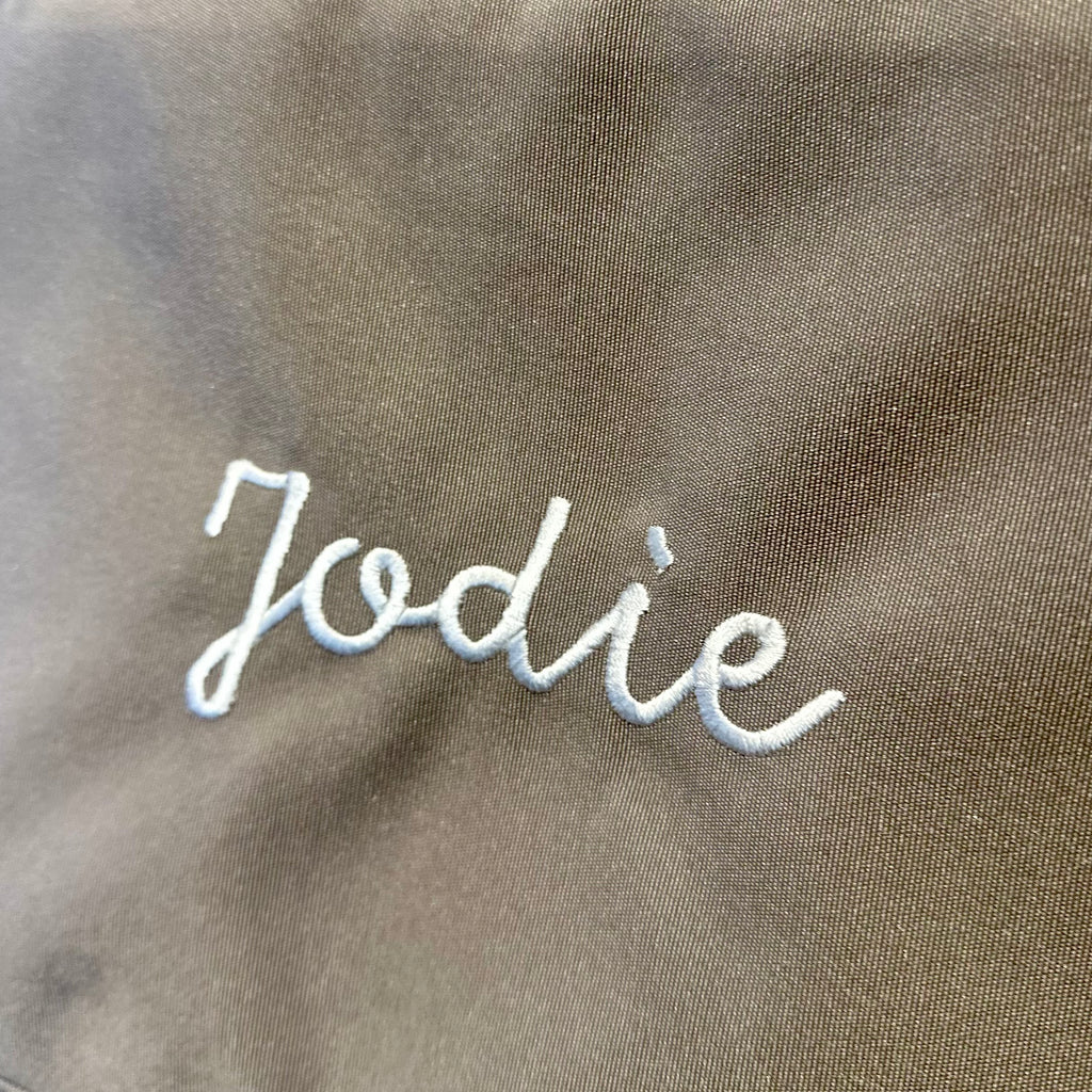 Text 'Jodie' embroidered on a brown fabric background