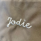 Text 'Jodie' embroidered on a brown fabric background