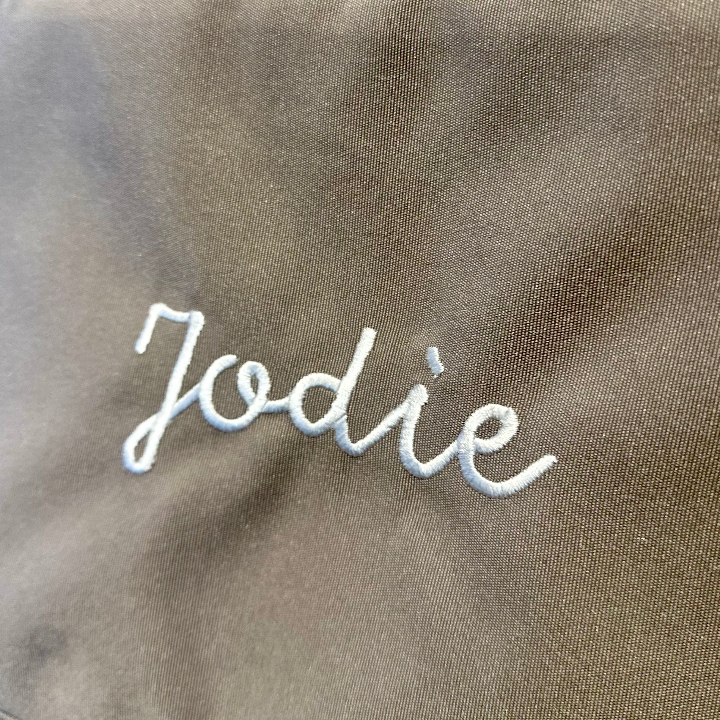 Text 'Jodie' embroidered on a brown fabric background