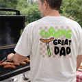 Man grilling outdoors wearing a t-shirt with 'Forking Great Dad' text and graphic.