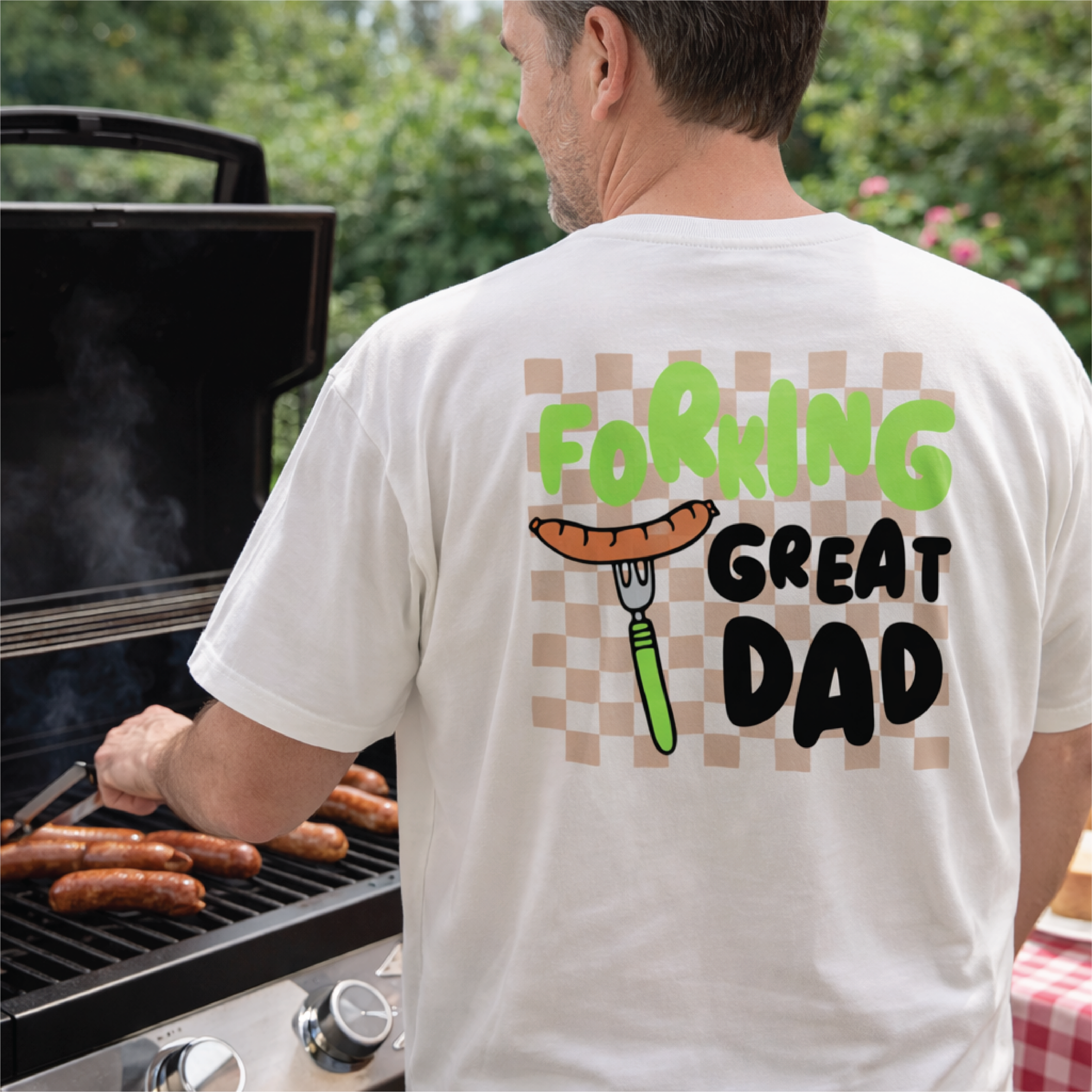 Man grilling outdoors wearing a t-shirt with 'Forking Great Dad' text and graphic.