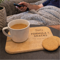 Person watching TV with a mug of coffee and cookies on a tray labeled 'Dad's Formula 1 Snacks'.