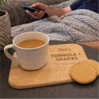 Person watching TV with a mug of coffee and cookies on a tray labeled 'Dad's Formula 1 Snacks'.