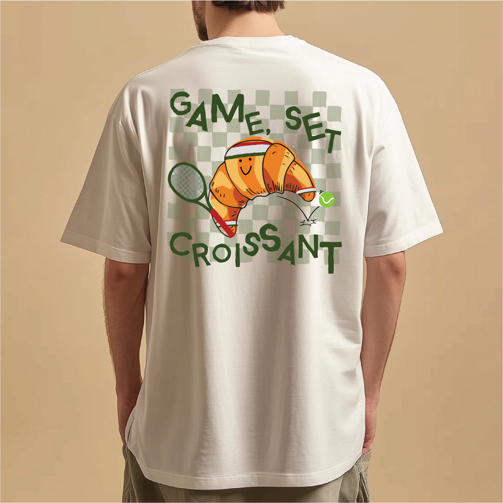 White t-shirt with a croissant graphic and text on the back, worn by a person against a beige background.