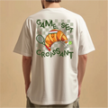 White t-shirt with a croissant graphic and text on the back, worn by a person against a beige background.
