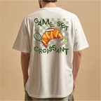 White t-shirt with a croissant graphic and text on the back, worn by a person against a beige background.