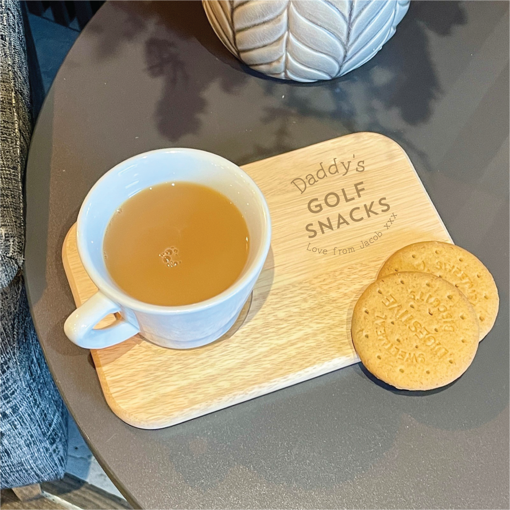 Cup of tea and cookies on a wooden board with 'Daddy's Golf Snacks' engraving.