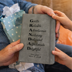 Two people holding a grey grandad notebookk with personalized text on a blurred background
