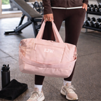 Person holding a pink duffel bag with initials in a gym setting