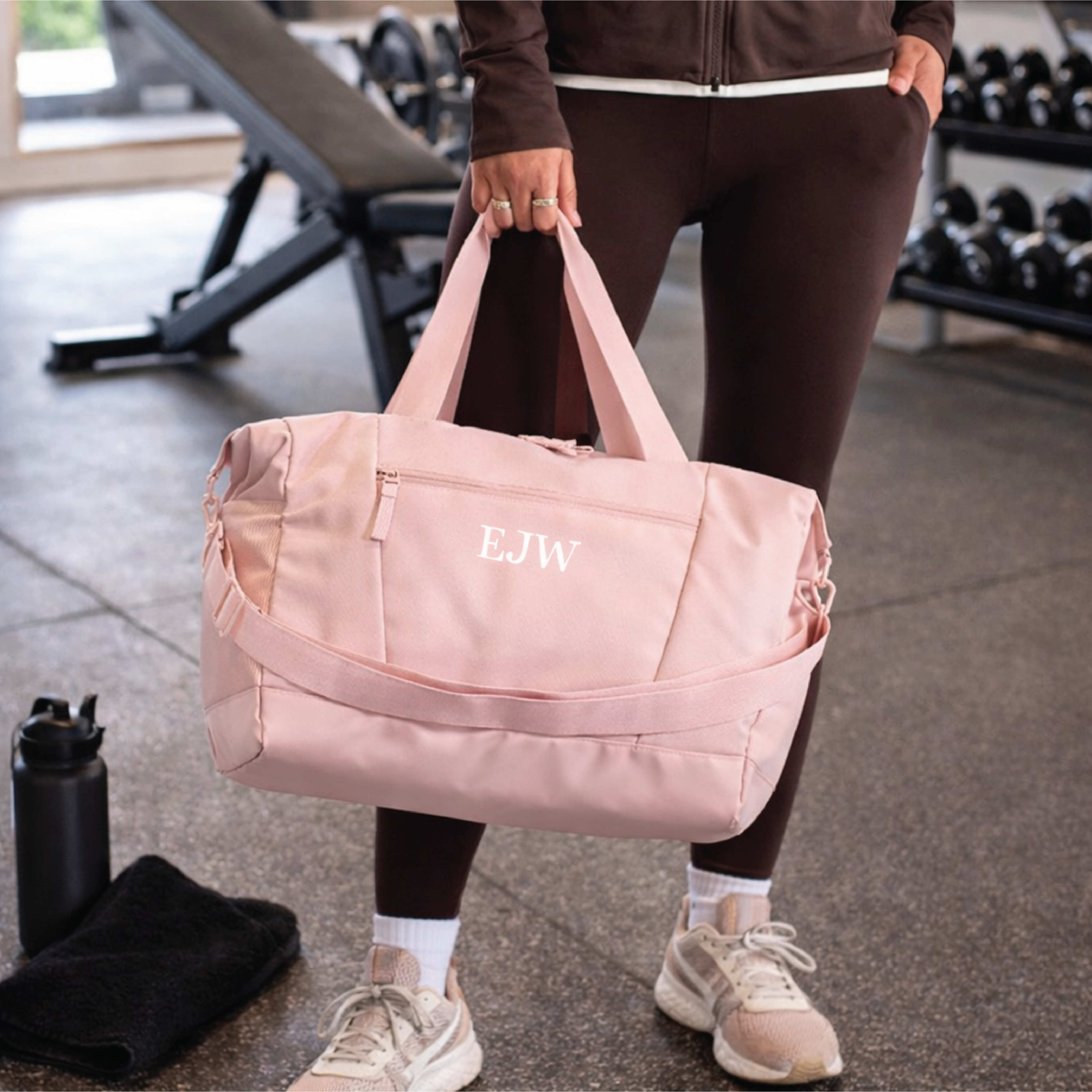 Person holding a pink duffel bag with initials in a gym setting