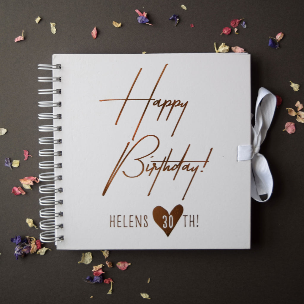 White spiral-bound notebook with 'Happy Birthday! Helens 30th!' text on a dark background with dried flowers.