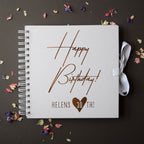 White spiral-bound notebook with 'Happy Birthday! Helens 30th!' text on a dark background with dried flowers.