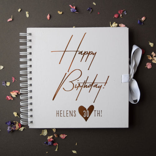 White spiral-bound notebook with 'Happy Birthday! Helens 30th!' text on a dark background with dried flowers.