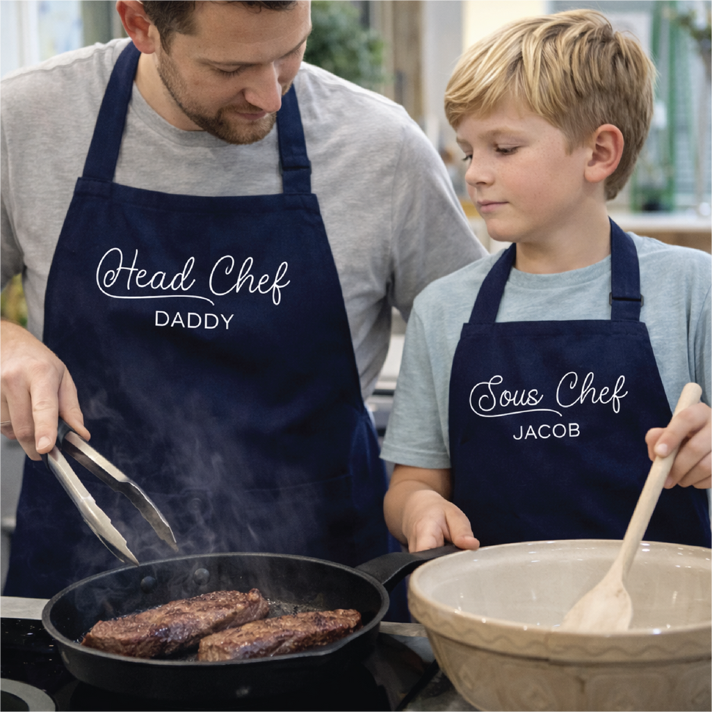 Man and young boy cooking together, wearing aprons labeled 'Head Chef Daddy' and 'Sous Chef Jacob'.