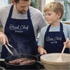 Man and young boy cooking together, wearing aprons labeled 'Head Chef Daddy' and 'Sous Chef Jacob'.