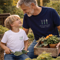 Man and child in a garden setting with potted plants, wearing matching t-shirts.