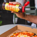 Person drizzling honey over a pizza from a bottle labeled 'Honey Bunches of Honey'.