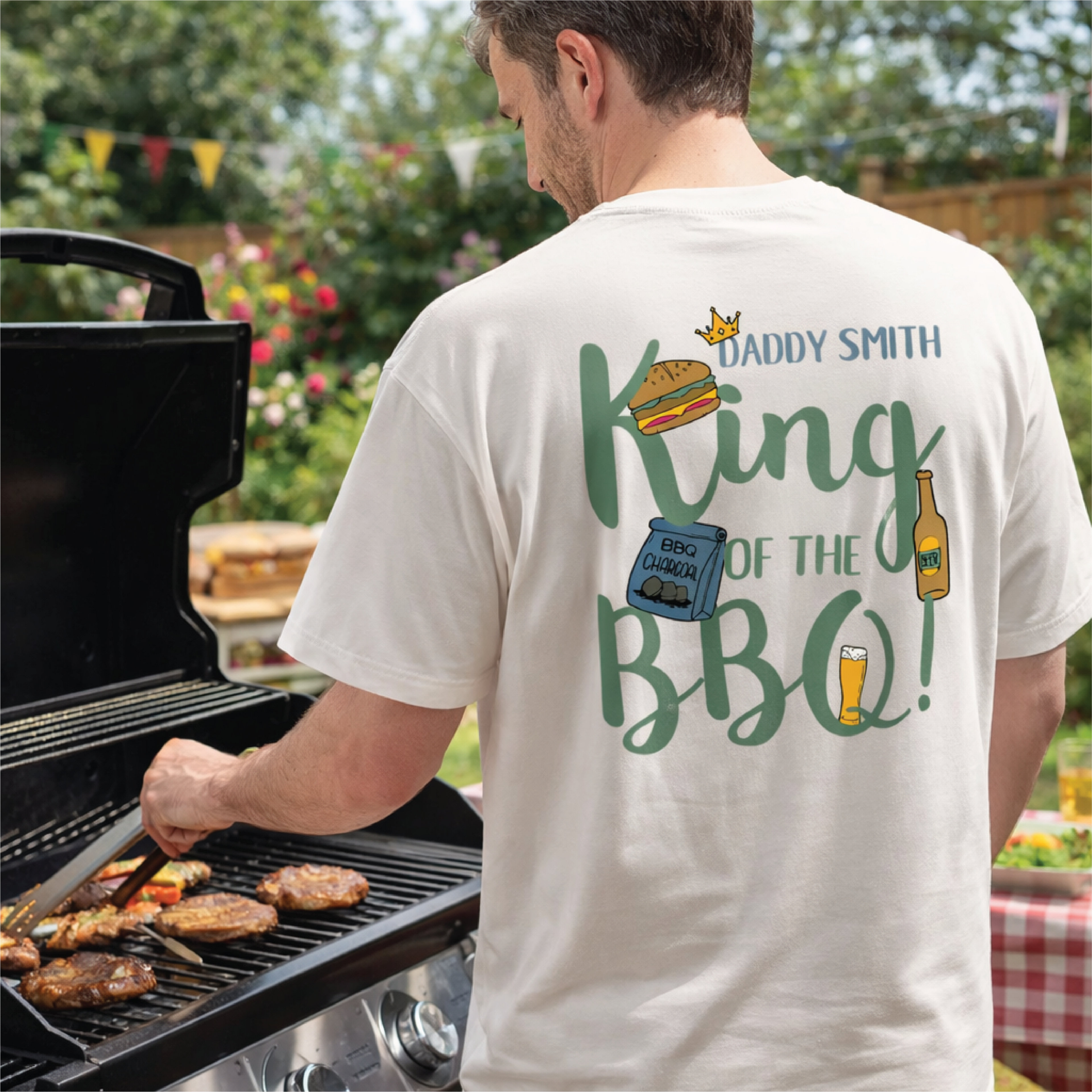 Man grilling outdoors wearing a t-shirt with 'Daddy Smith King of the BBQ!' text and graphics.