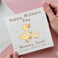 Card with 'Happy Mother's Day' and 'Mummy Duck!' text, held by a hand on a pink background.