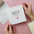 Card with 'Happy Mother's Day Nummy to be' text held by hands on a pink background