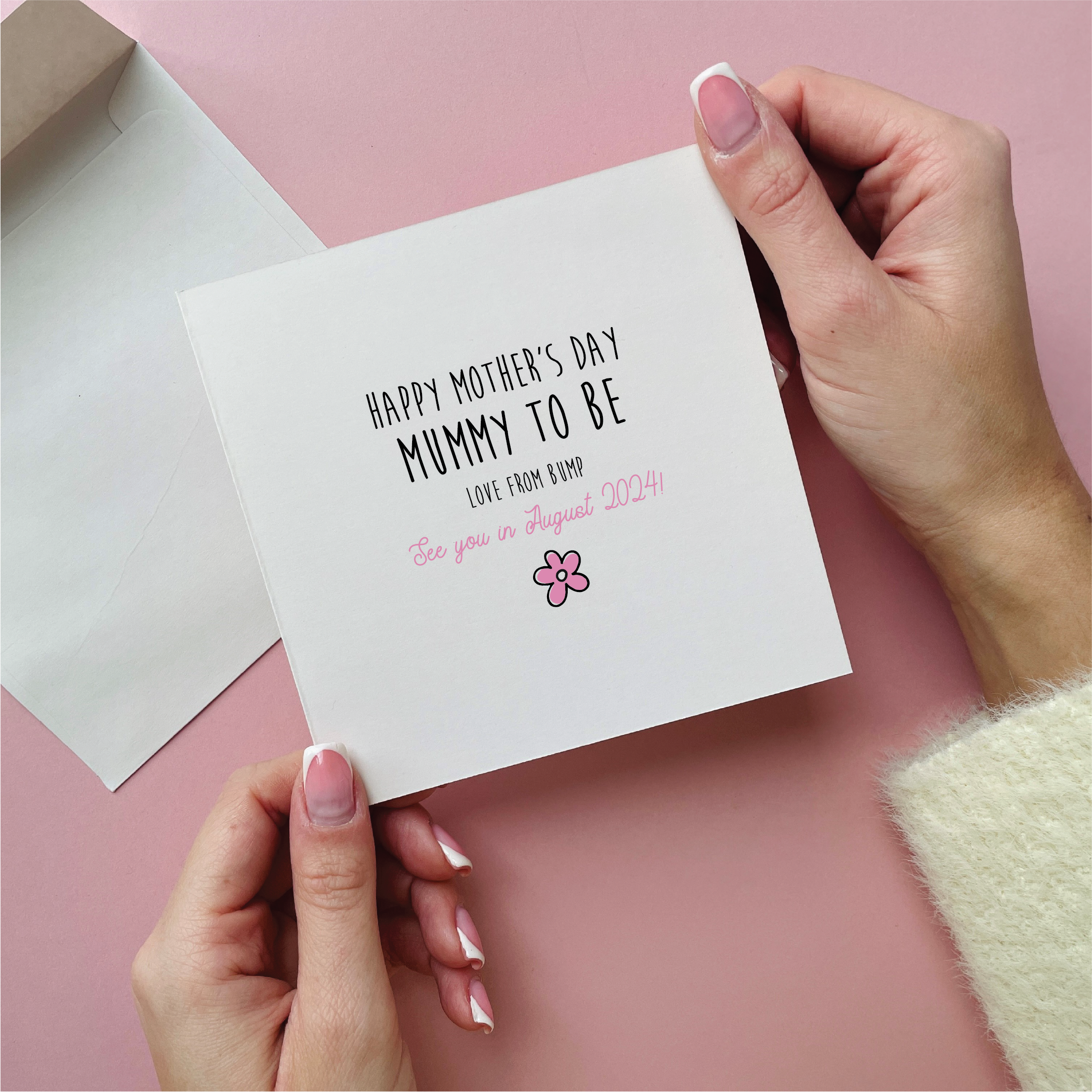 Card with 'Happy Mother's Day Nummy to be' text held by hands on a pink background