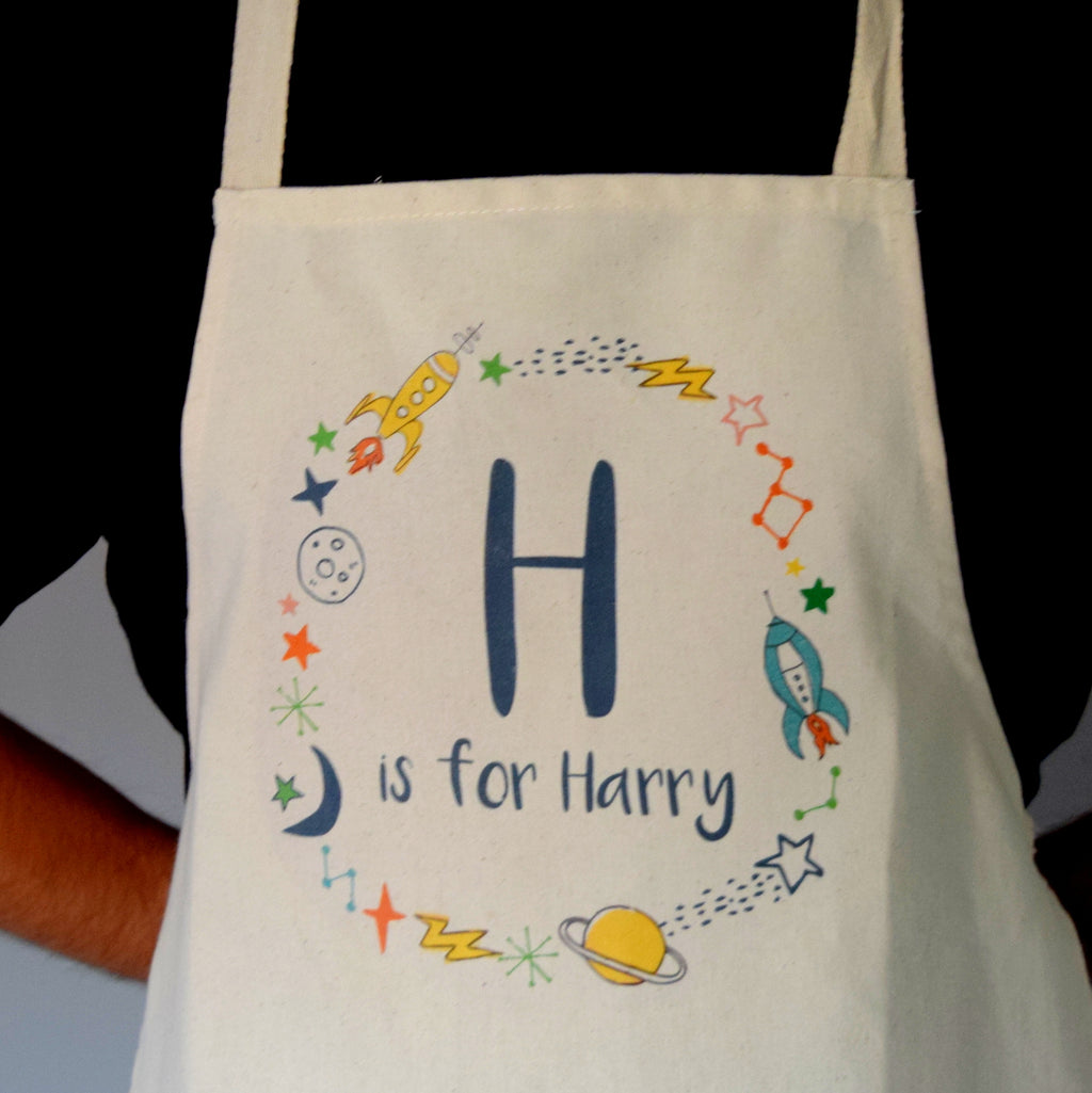White apron with space-themed design and 'H is for Harry' text