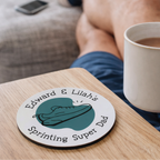 Person holding a mug with a coaster featuring 'Edward & Lillah's Sprinting Super Dad' on a table. The perfect coaster for a runner dad. 