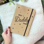 Notebook with 'Best Daddy Ever!' text held by a hand on a textured surface.