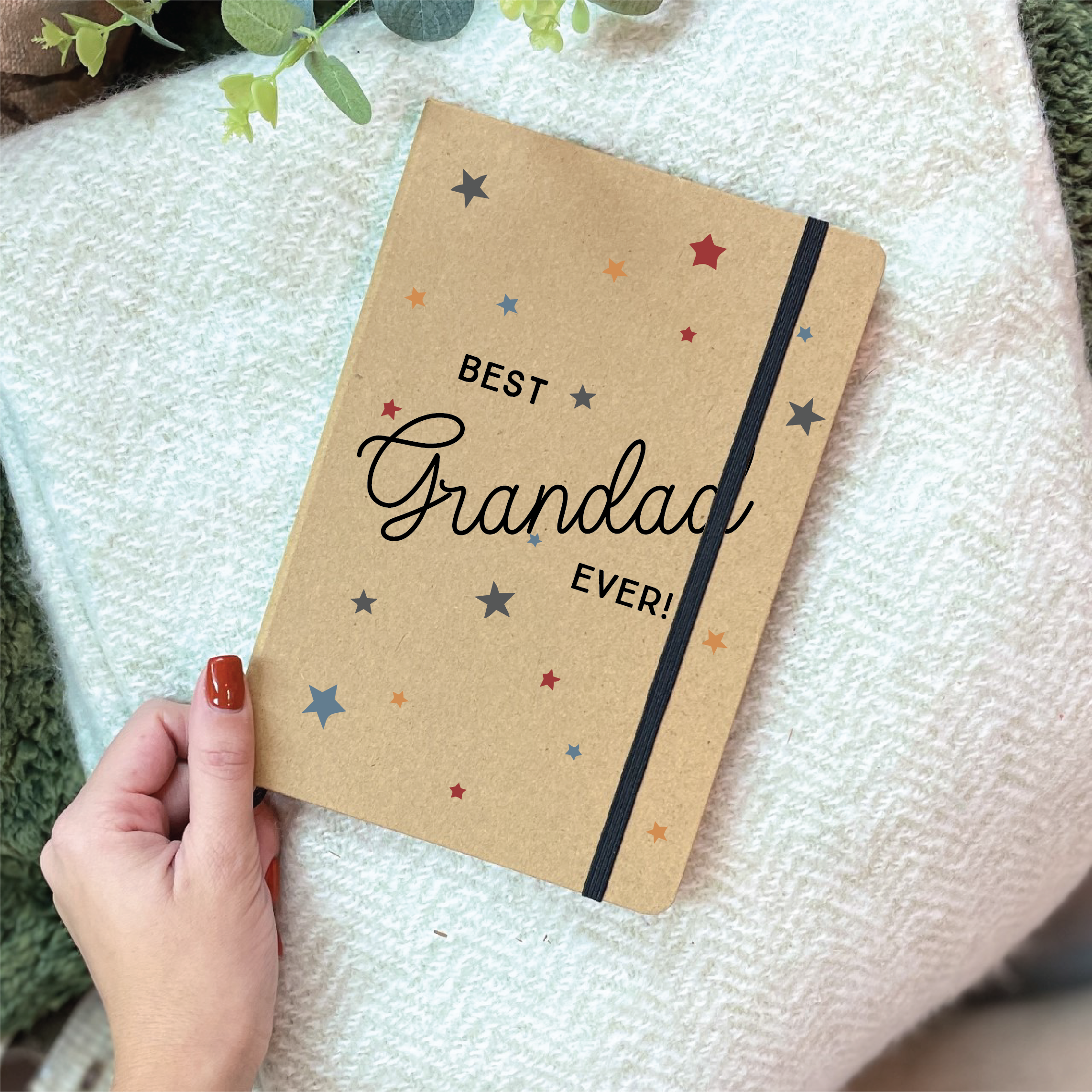 Notebook with 'Best Grandad Ever!' text held by a hand on a textured surface.