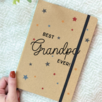 Notebook with 'Best Grandpa Ever!' text held by a hand on a textured surface.