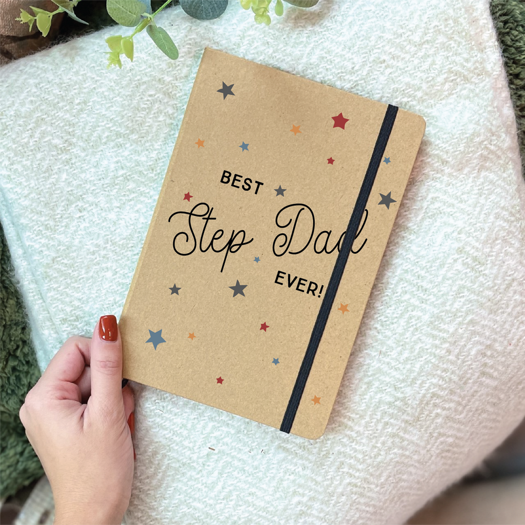 Notebook with 'Best Step Dad Ever!' text held by a hand on a textured surface.