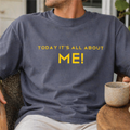 Person wearing a t-shirt with 'TODAY IT'S ALL ABOUT ME!' text, sitting outdoors.