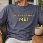 Person wearing a t-shirt with 'TODAY IT'S ALL ABOUT ME!' text, sitting outdoors.