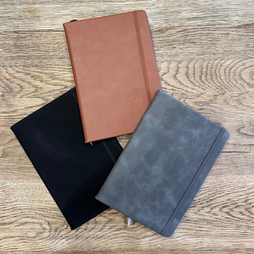 Three notebooks in black, brown, and gray on a wooden surface