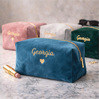 Blue makeup bag with 'Georgia' and a heart embroidered on it, surrounded by other bags and a lipstick.