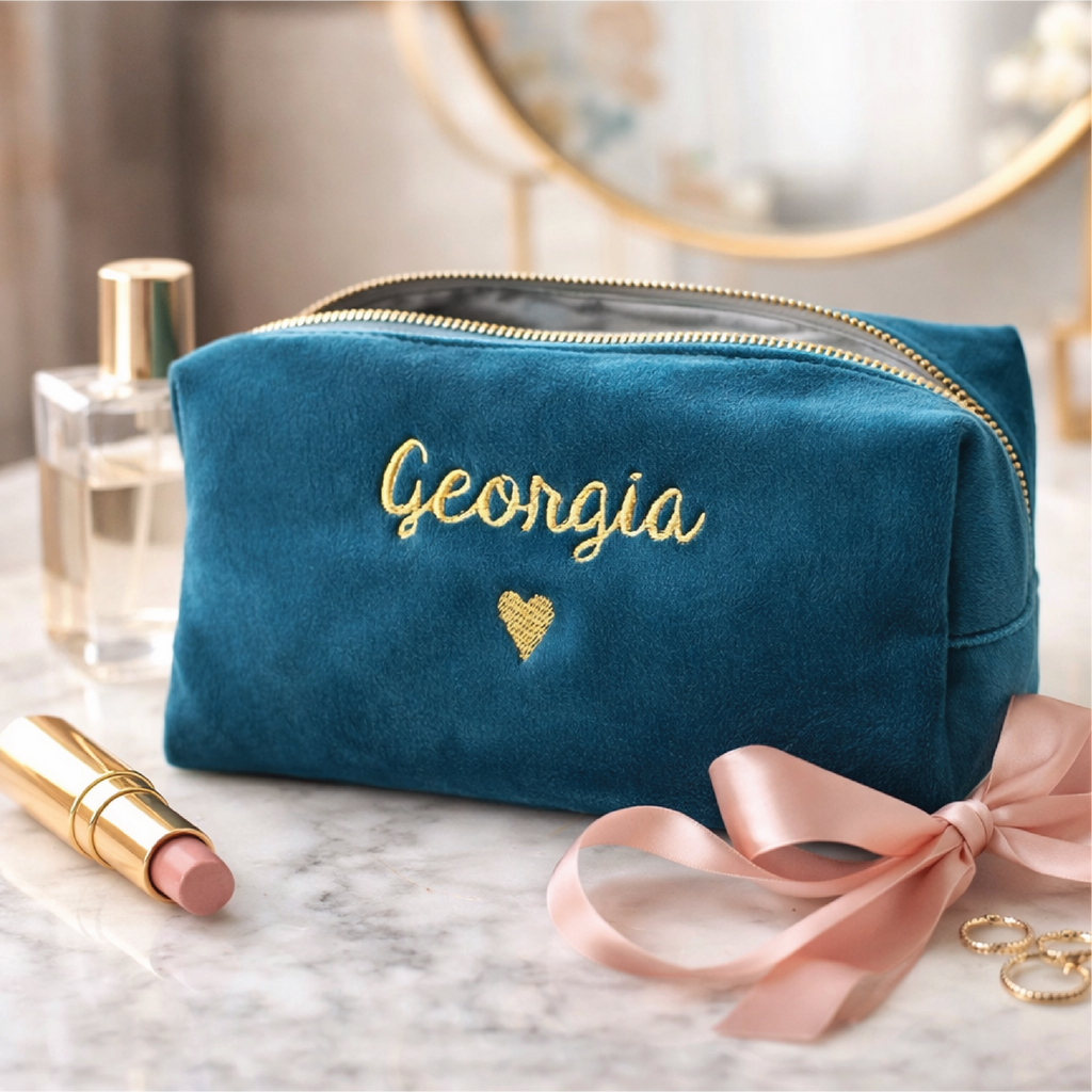 Blue makeup bag with 'Georgia' embroidery on a marble surface with lipsticks and perfume.